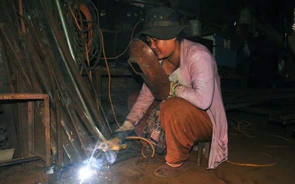 Une apprentie soude un morceau de métal en portant un masque de protection