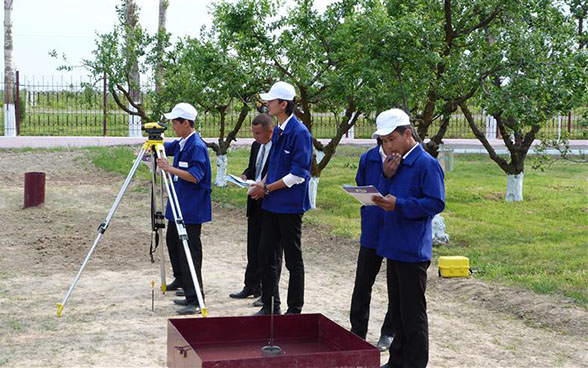 Apprentices standing in a park learn how to use a theodolite