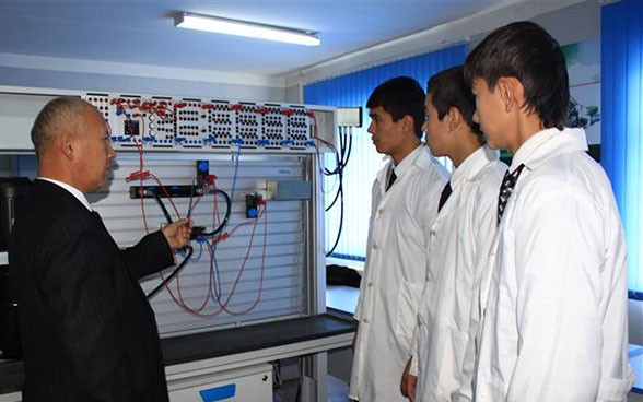 Un enseignant et trois apprentis devant un panneau électrique