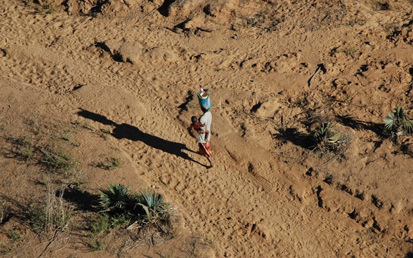 Frau läuft in Wüste mit Kind auf dem Arm.