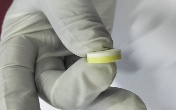 A man holding an ASAQ antimalarial tablet between finger and thumb. The drug is manufactured at the new site in Tanzania.