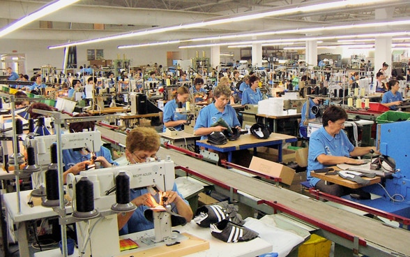 Blick in eine Fabrikhalle in Bosnien-Herzegowina, in der zahlreiche Frauen an Nähmaschinen Schuhe nähen.