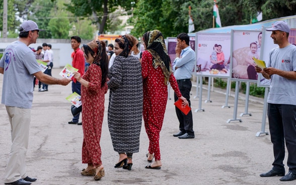 In Tadschikistan nehmen Fussgängerinnen nehmen gedrucktes Informationsmaterial entgegen. 