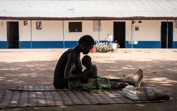 Une jeune mère porte son enfant sous-alimenté devant un centre de stabilisation soutenu par l’UNICEF à Malualkon, Aweil, Soudan du Sud.  