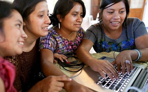 Quatre femmes travaillent sur un ordinateur portable dans une ambiance détendue.