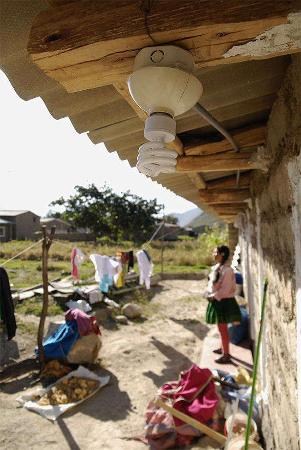 A low-energy light bulb hangs from the eaves of a house.  A girl is standing in the background.