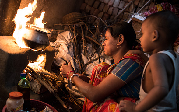 An Indian woman is preparing food on a cooker. A child is standing next to her. 