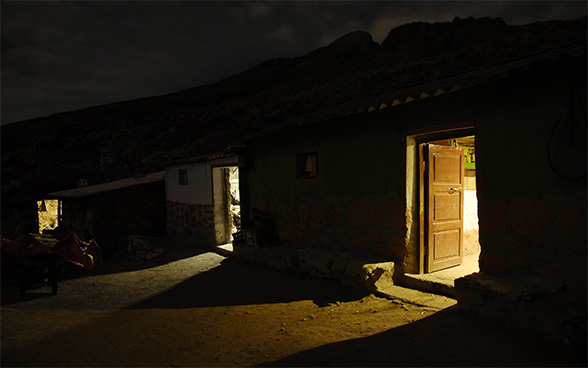 A house with three open doors at night. A light is burning inside the house.