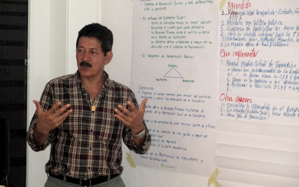 Ein Vertreter der Delegation aus Honduras steht vor einem Plakat, auf dem seine Erkenntnisse aus dem Austausch mit den Schweizer Bildungsvertreterinnen und Bildungsvertretern notiert sind.
