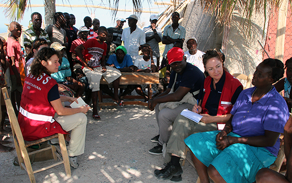 Zwei Schweizer Expertinnen hören gemeinsam mit anderen Lokalbewohnern einer Haitianerin zu.