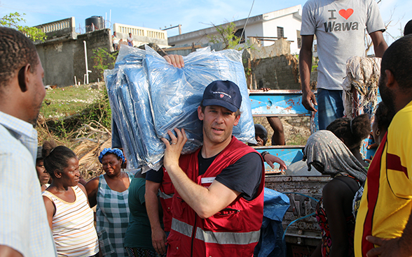 Ein von Haitianern umgebener Schweizer Experte verteilt Planen.