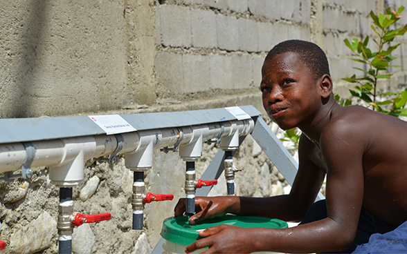 Ein Junge trinkt an einem von der Humanitären Hilfe der DEZA installierten Wasserhahn und füllt einen Behälter.