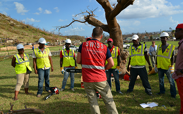 A Swiss expert holding a chainsaw instructs members of the Haitian civil protection authorities.