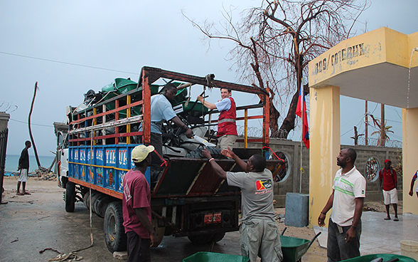Männer entladen einen mit Schubkarren und Werkzeug beladenen Lastwagen. 