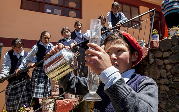 A boy handles a scientific instrument as other children watch.