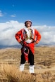 A man in traditional Peruvian clothing stands in open countryside in the Peruvian highlands, and looks up at the sky.