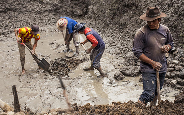 Quattro uomini lavorano con le vanghe in una sorgente d’acqua.