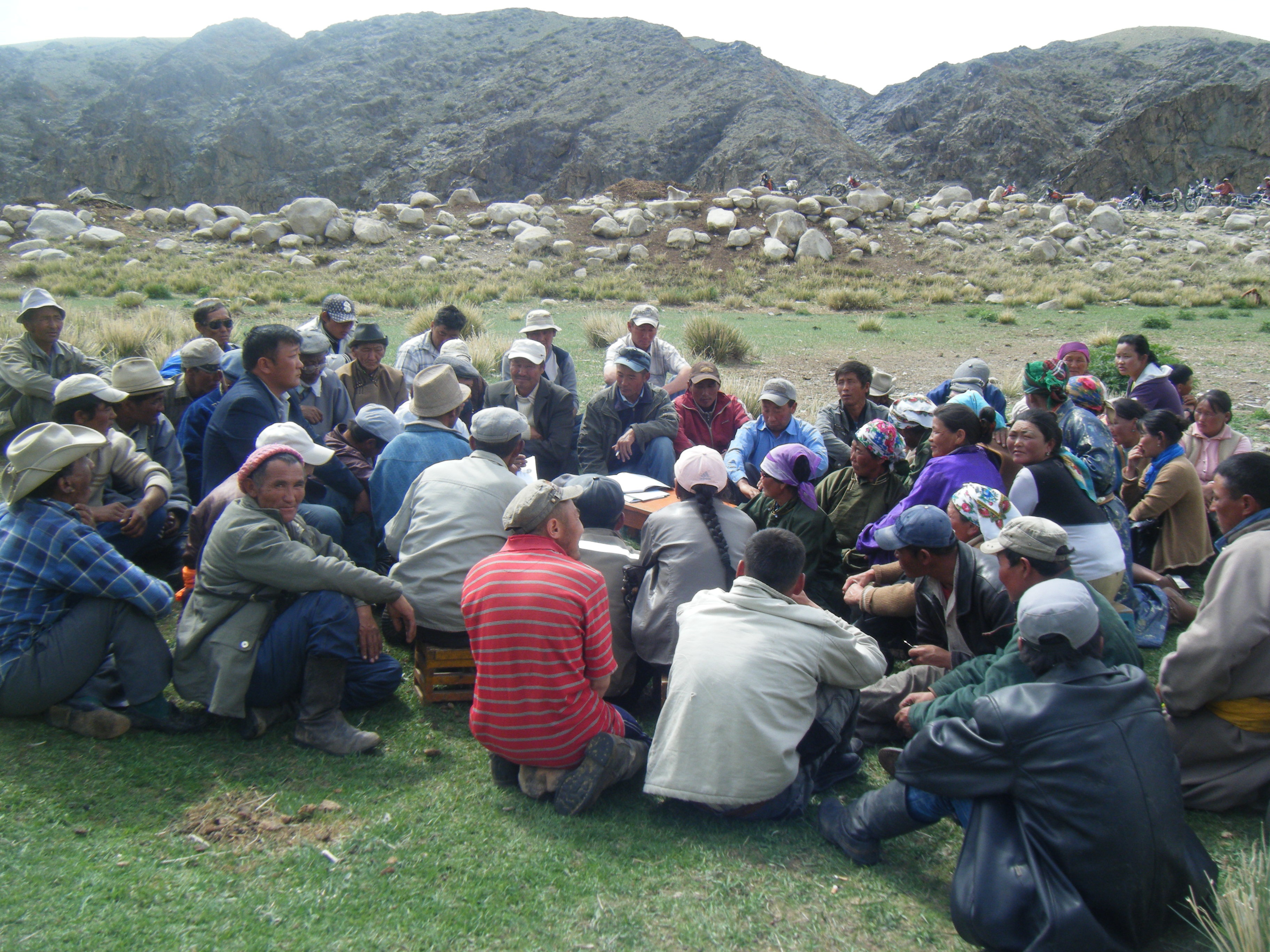 Group of herders sitting on the grass, engaged in discussion.