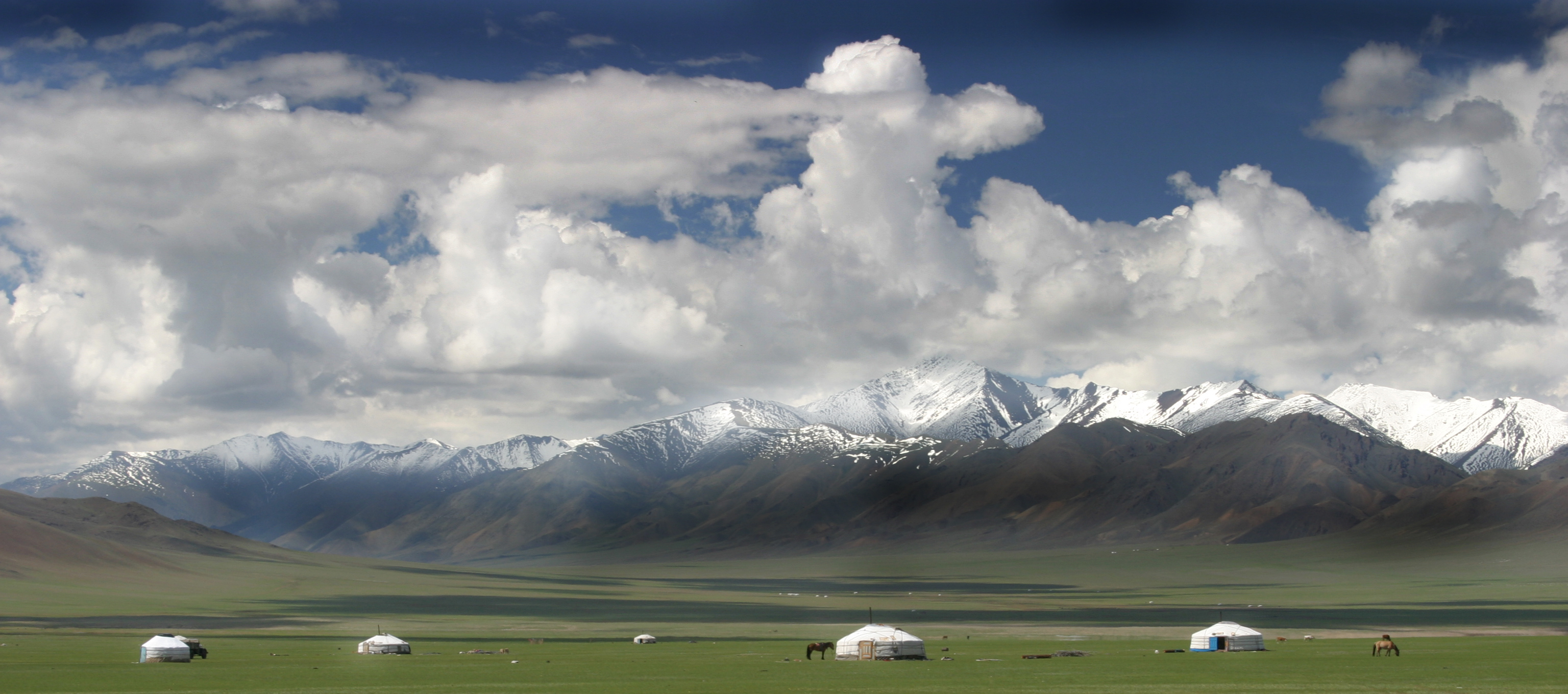 Yurts dotting a grassy plain against the backdrop of a mountain range.