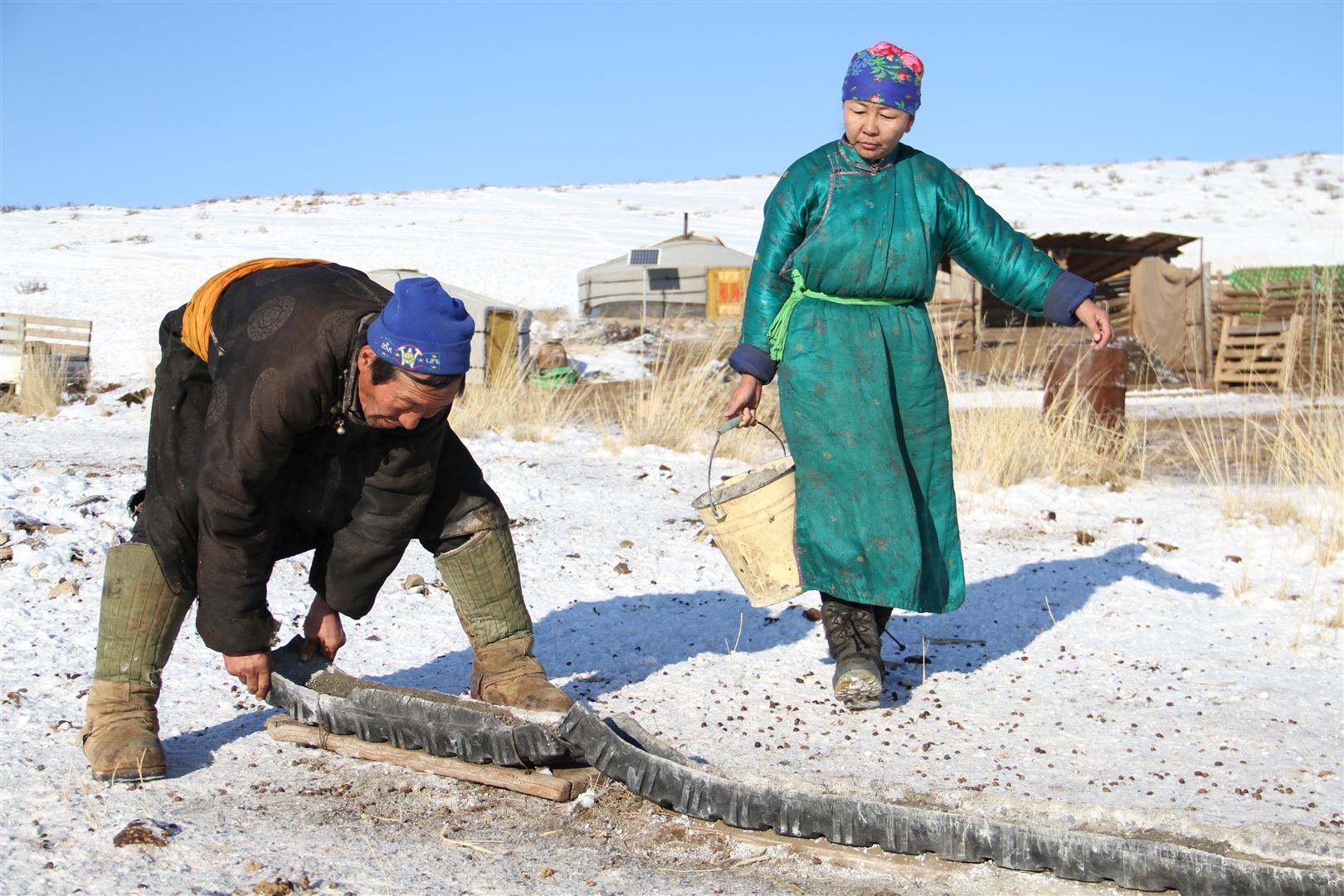 A man setting up a trough and a woman carrying a bucket of water to fill it.