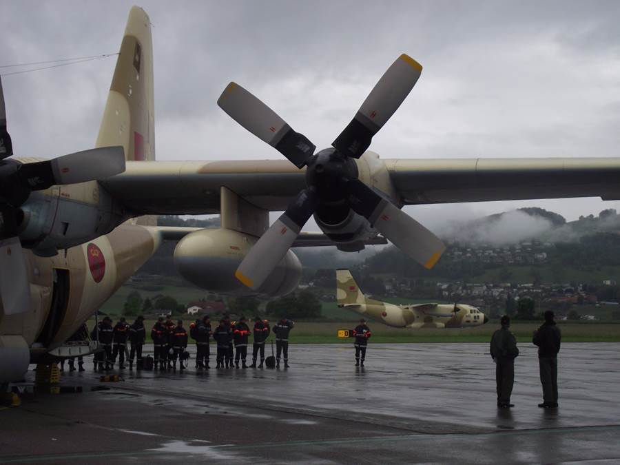 two Moroccan military aircraft on the tarmac at Bern airport. Beside them is a group of rescue workers preparing their things. 