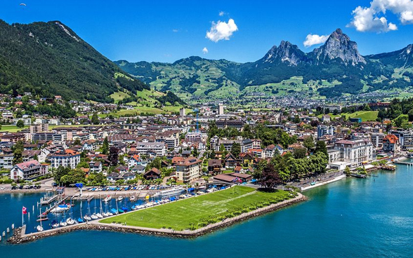 Ansicht der Stadt Brunnen von oben mit dem gut sichtbaren Auslandschweizerplatz, dem See und den Bergen im Hintergrund. 