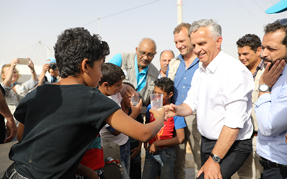 Un giovane profugo siriano porge un bicchiere d’acqua al consigliere federale Didier Burkhalter.