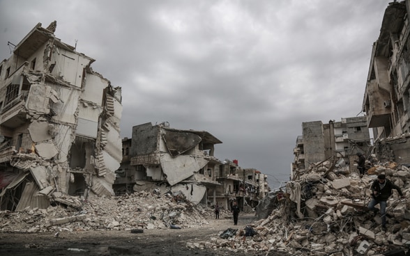 Menschen gehen durch die Trümmer der von Luftangriffen getroffenen syrischen Stadt Idlib. 