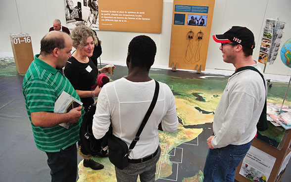 Trois visiteurs écoutent une collaboratrice de la DDC sur le stand. © DFAE