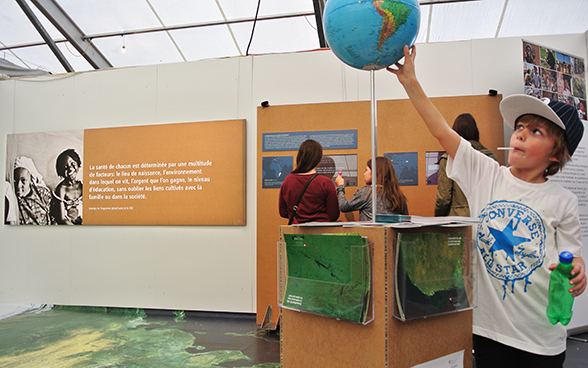 Au premier plan, un jeune garçon étudie une mappemonde installée sur le stand de la DDC. © DFAE