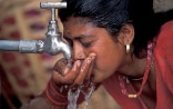 Une femme boit de l‘eau d’un robinet.