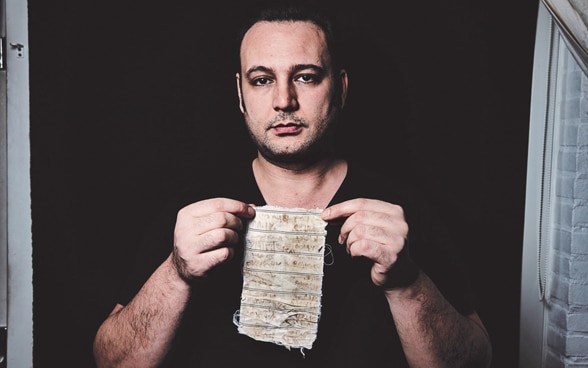 A man holds a piece of cloth and looks into the camera