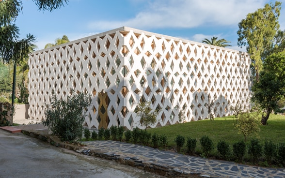 Outside view of the Swiss embassy in Algiers. The building is a white rectangular cube. The façade consists of a large lattice design of intersecting beams. 