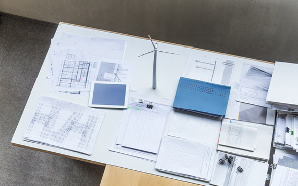 Wind power plant model, design plans and tablet on the table in the office.