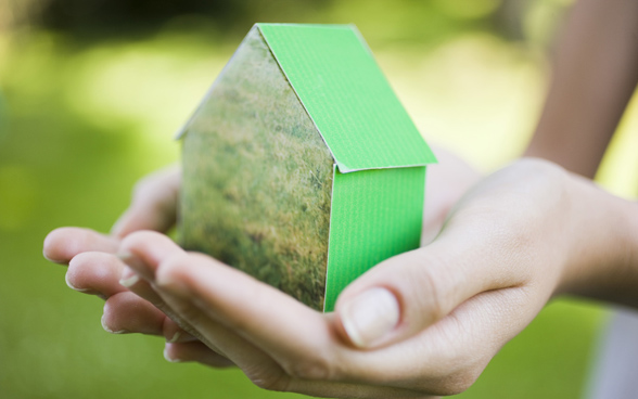 Due mani racchiudono una casetta verde di cartone.