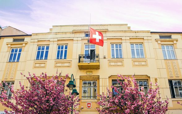 A building with a Swiss flag and two trees in the foreground, the Swiss embassy.