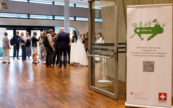 Image of an embassy event with a poster featuring the Green Swiss pocket knife logo. 