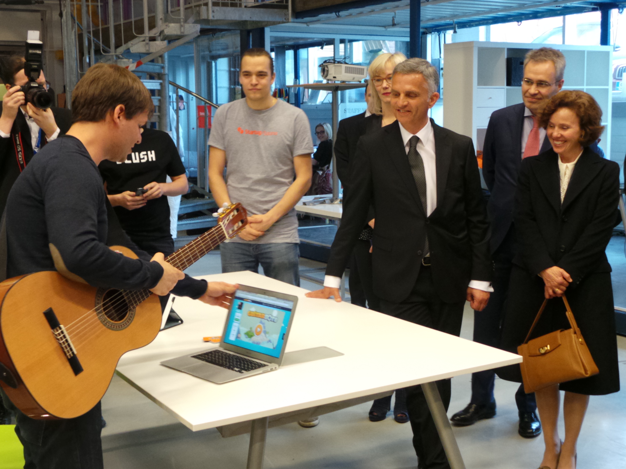 A Swiss explains a computer program on learning to play the guitar to President Didier Burkhalter and his wife. 