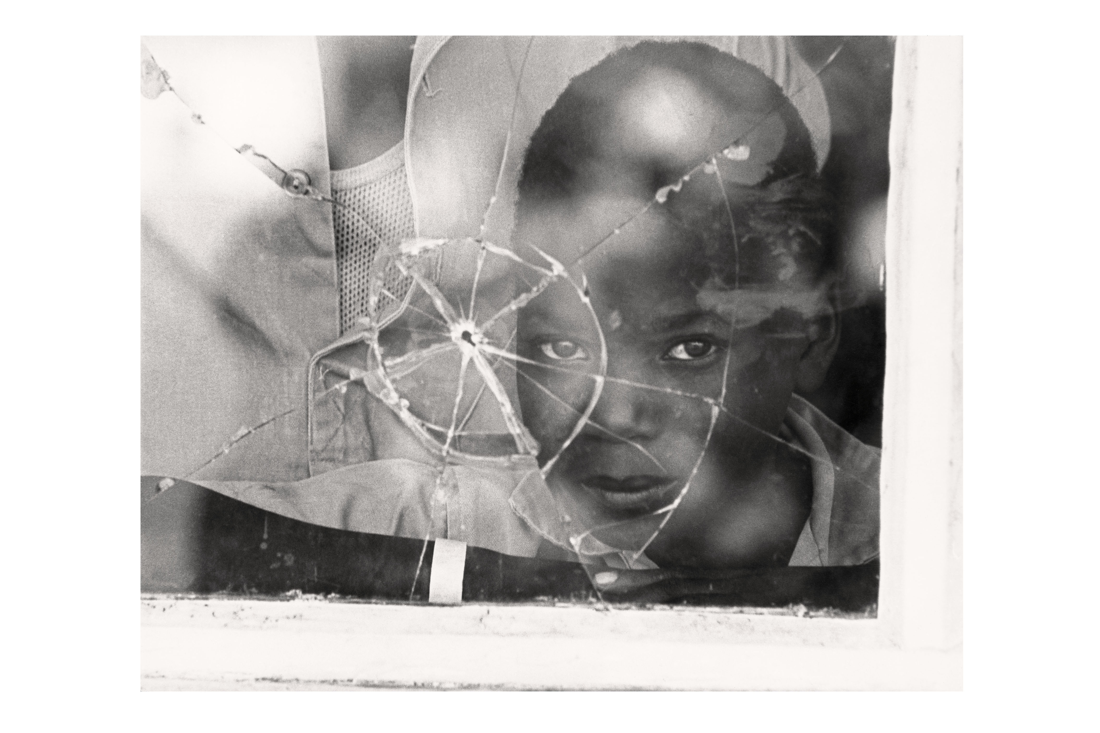 A Mozambican boy looks through a window with a bullet hole 