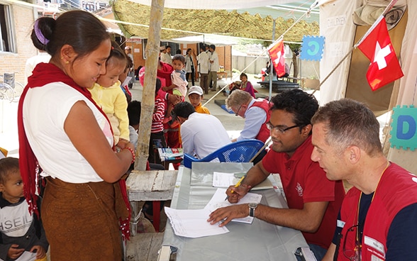 Collaboratori dell'Aiuto umanitario della Confederazione mostrano qualcosa su un documento a una donna nepalese.