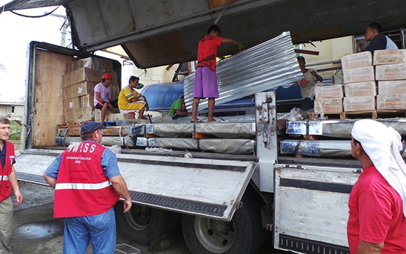 Membri del Corpo svizzero di aiuto umanitario scaricano, insieme agli abitanti dell’isola di Leyte nelle Filippine, un camion con merci dell’Aiuto umanitario