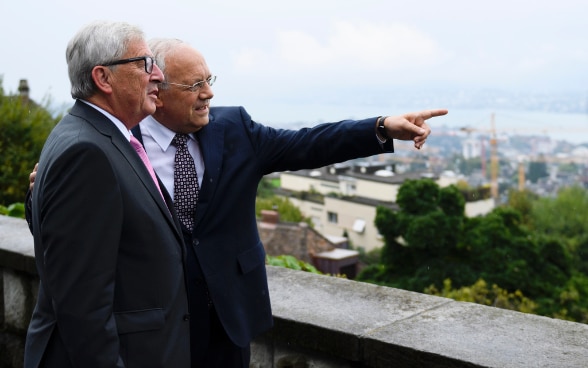  Le président de la Confédération Johann N. Schneider-Ammann se tient à côté du président de la Commission européenne Jean-Claude Juncker sur la terrasse de la Villa Hatt à Zurich et montre du doigt la ville au loin.