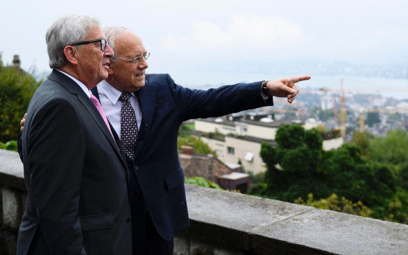 President of the Swiss Confederation, Johann N. Schneider-Ammann, standing next to the President of the European Commission, Jean-Claude Juncker, on the terrace of Villa Hatt in Zurich pointing a finger in the direction of the city.