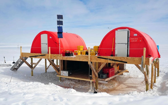 Une station de recherche suisse dans la région arctique, composée de deux tentes rouges posées sur un plateforme en bois.