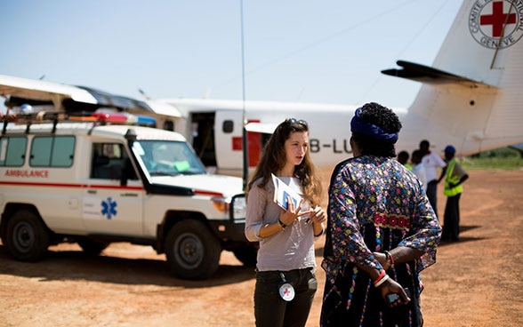 A young woman speaks to a patient in front of an ICRC plane on the tarmac in Torit.