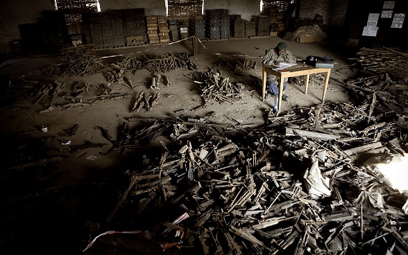 Ein kongolesischer Soldat, der an einem Tisch sitzt, zählt die Waffen eines Waffen- und Munitionslagers.