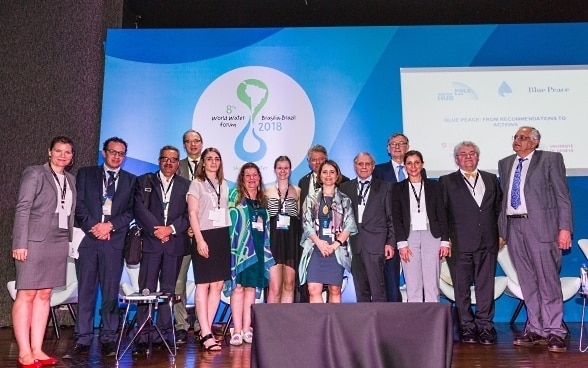 Sechs Frauen und neun Männer verschiedener Nationalitäten vor einer blauen Stellwand mit dem Logo des World Water Forums in Brasilia.