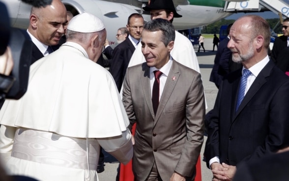 Il Papa stringe la mano a Ignazio Cassis davanti a un aereo Alitalia. Al suo fianco siedono il Presidente Berset e il Presidente del Consiglio nazionale de Buman.