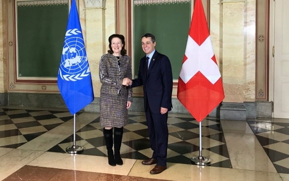 Bundesrat Cassis schüttelt Henrietta Fore die Hand. Im Hintergrund sind die Flaggen der Schweiz und der UNO zu sehen. 