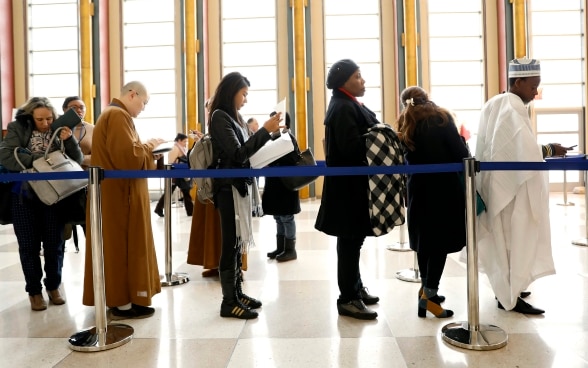 Frauen und Männer warten auf die Registrierung in einer hohen Halle.